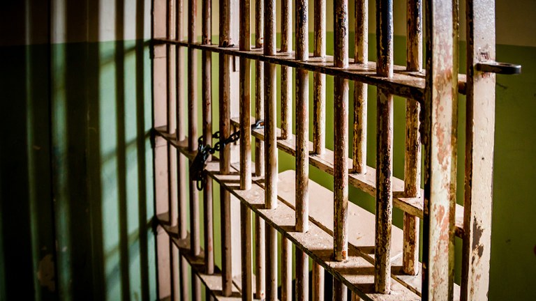 Stock image depicting the barred doors of a prison cell with a chain and lock.